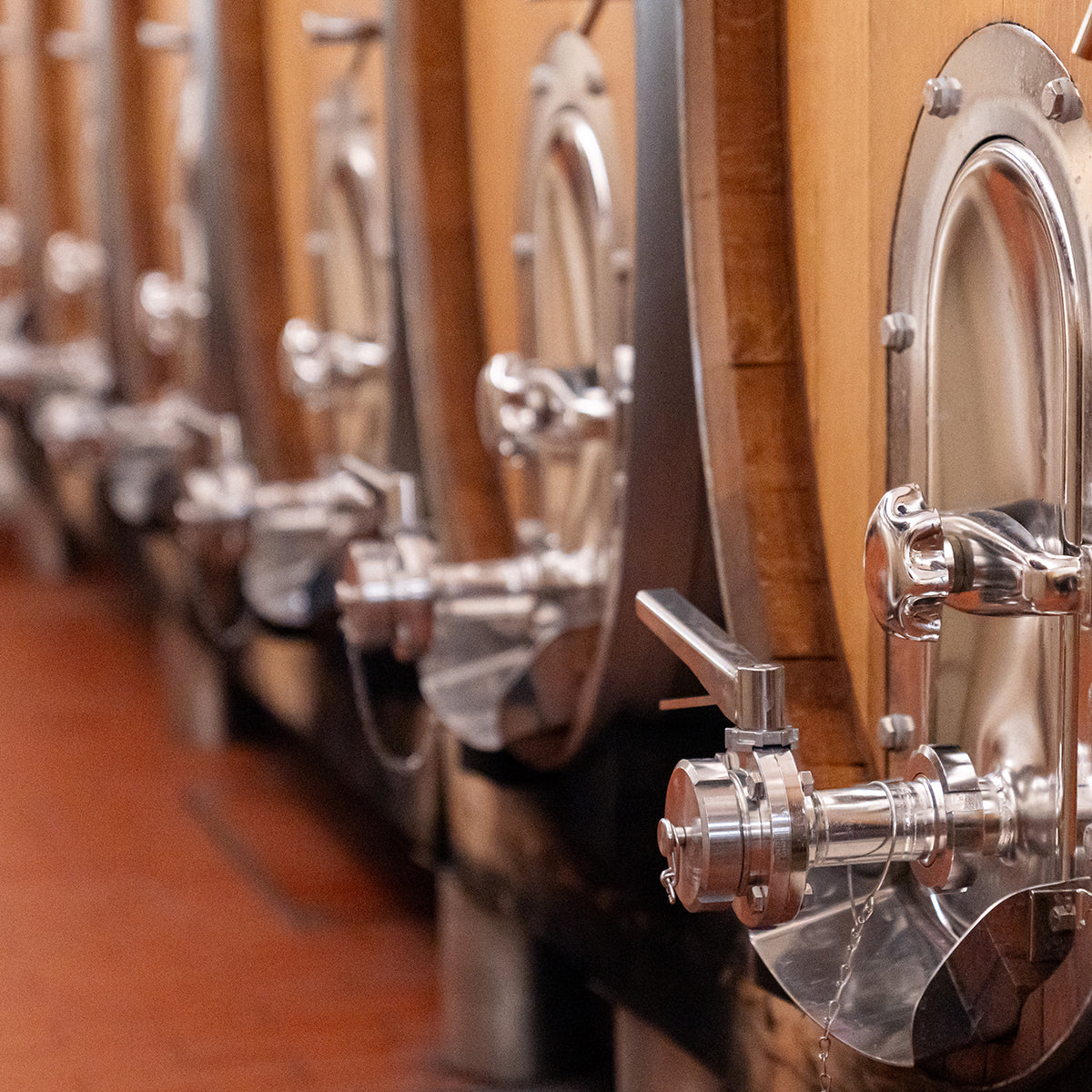 Edelstahltanks und Holzfässer in der Weinproduktion der WZG mit sichtbaren Armaturen und Auslässen.