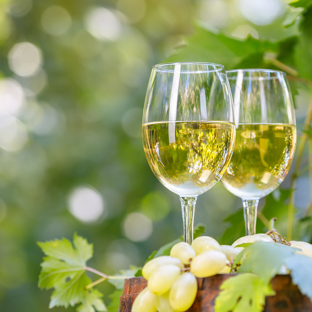 Zwei Gläser Weißwein der Serie Aus'm Ländle neben hellen Weintrauben in grüner Naturkulisse.