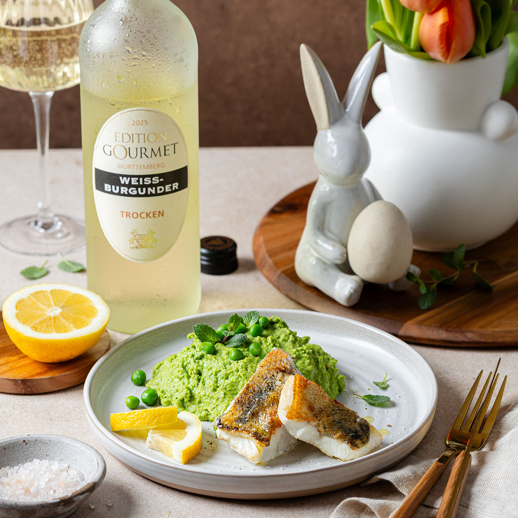 Edition Gourmet Weissburgunder der WZG mit Weinglas und fein angerichtetem Gericht auf einem gedeckten Tisch.