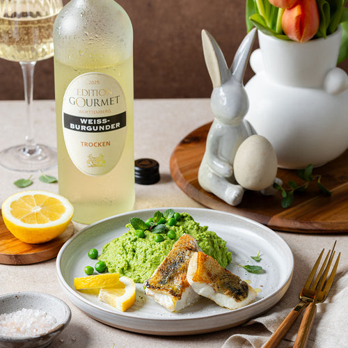 Edition Gourmet Weissburgunder der WZG mit Weinglas und fein angerichtetem Gericht auf einem gedeckten Tisch.