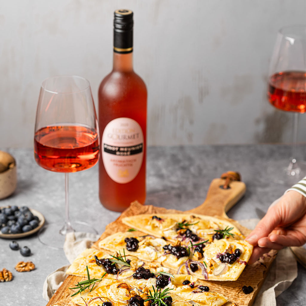 Edition Gourmet Roséwein der WZG mit gefülltem Weinglas und Flammkuchen auf einem gedeckten Tisch.
