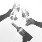 Mehrere Personen stoßen in Schwarz-Weiß mit Weingläsern an, während eine Flasche Edition Gourmet Wein der WZG gehalten wird.