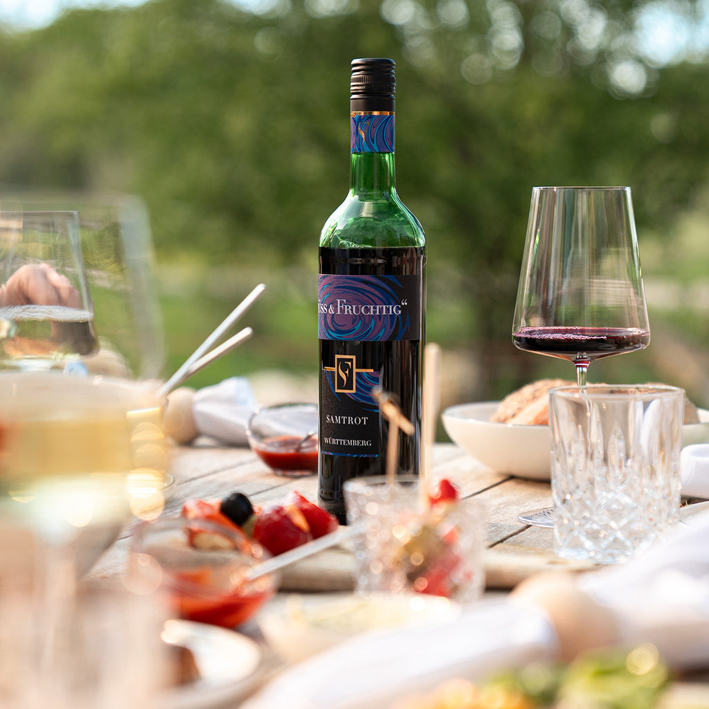 Süss & Fruchtig Rotwein Samtrot der WZG auf einem sommerlich gedeckten Tisch mit Speisen und Weingläsern.