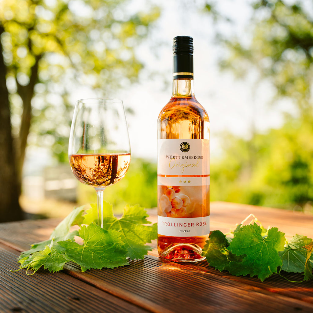 Trollinger Rose der WZG mit Weinglas auf einem Holztisch in sommerlicher Gartenatmosphäre.