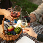 Mehrere Personen stoßen bei einem Picknick mit Wein aus dem Sortiment der WZG über einem Korb mit Snacks an.