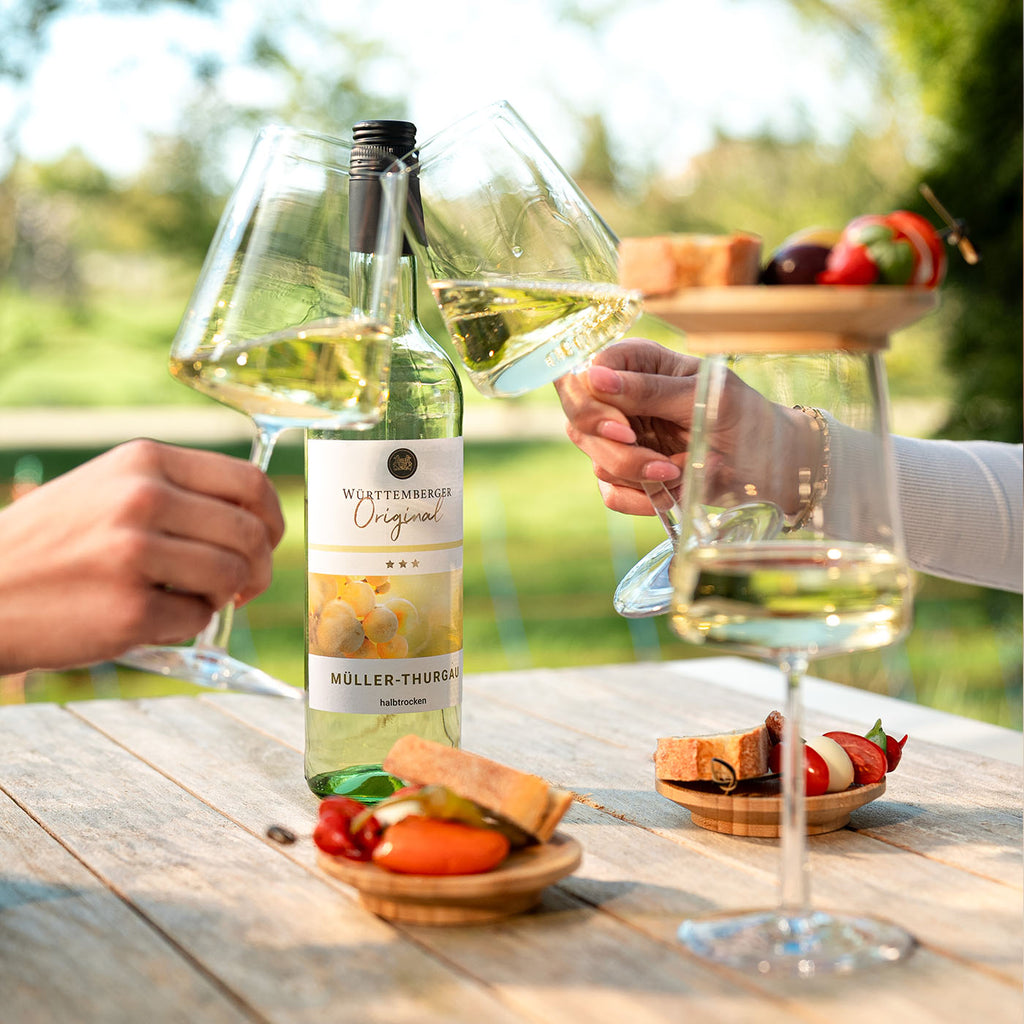 Württemberger Original Müller-Thurgau Weißwein der WZG mit mehreren Weingläsern und kleinen Speisen auf einem sommerlich gedeckten Tisch.