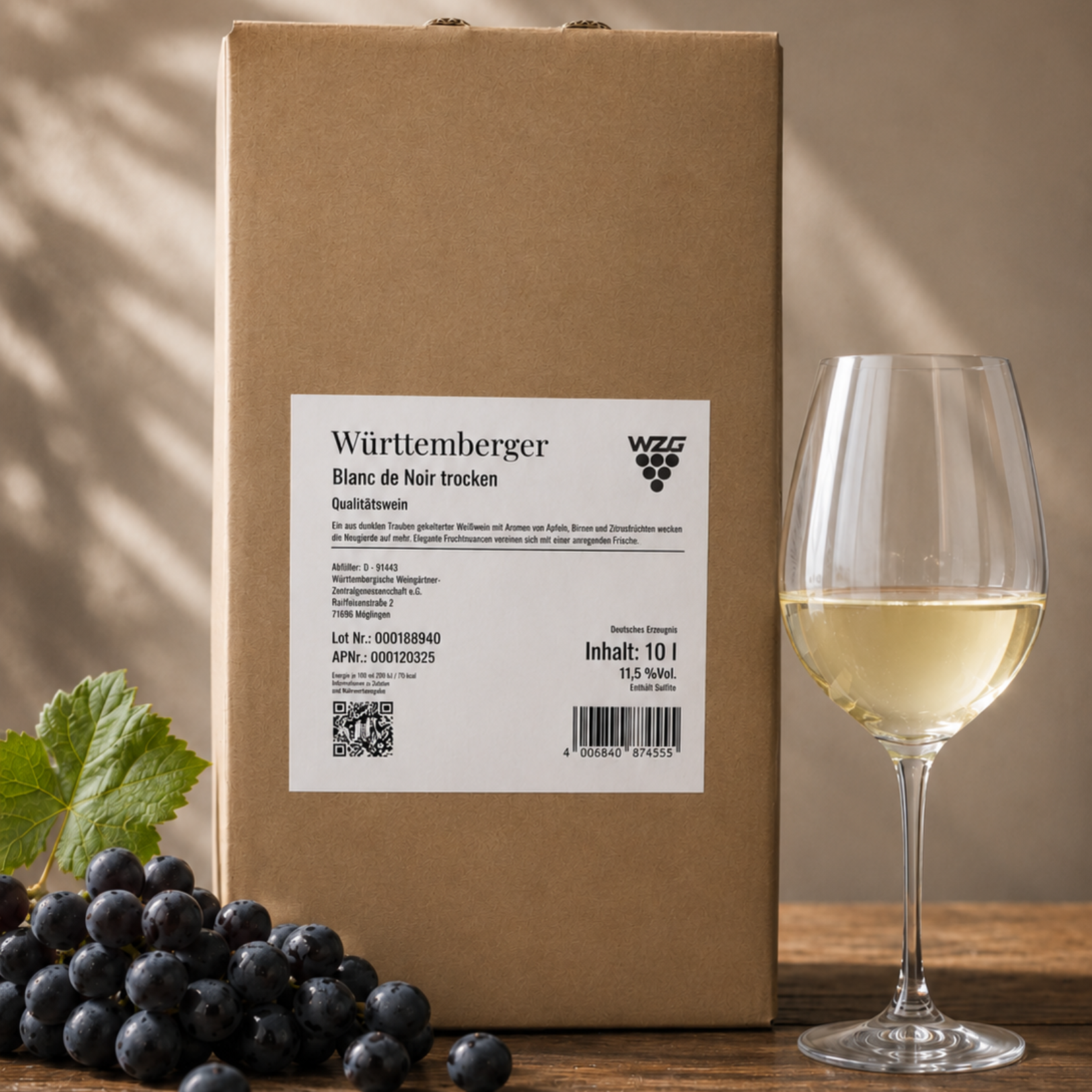 Württemberger Blanc de Noir im 10 Liter Bag in Box mit Weißweinglas und dunklen Trauben auf einem Holztisch.