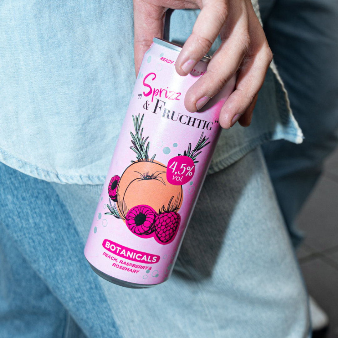 Person hält eine Dose Sprizz & Fruchtig Infusion Botanicals in der Hand. Mixgetränk auf Weinbasis mit Pfirsich, Himbeere und Rosmarin.